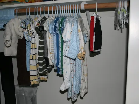 Baby bodysuits and sleepsuits hanging on small plastic hangers on a wardrobe rail.
