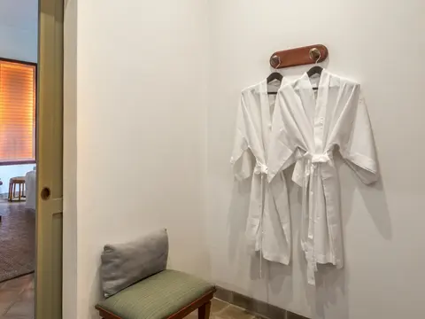 Two white bathrobes hanging on wooden hooks beside a bench and slippers in a spa changing room.
