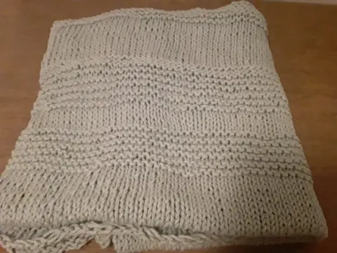 A chunky hand-knitted blanket lying folded on a wooden floor.