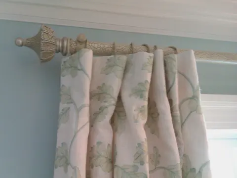 Embroidered linen curtains hanging from a decorative rod beside a window.