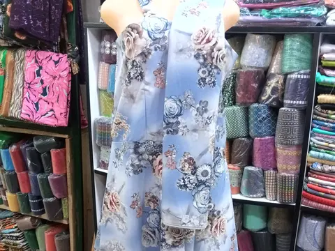 A light blue floral woven dress displayed on a headless dress form in a fabric shop.