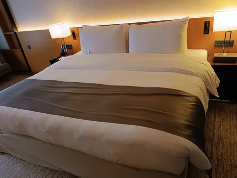 A wide bed with a plump white duvet and four pillows against a wooden headboard.