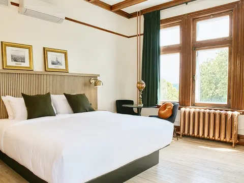 A bright hotel room with a neatly made white bed beside a tall window.