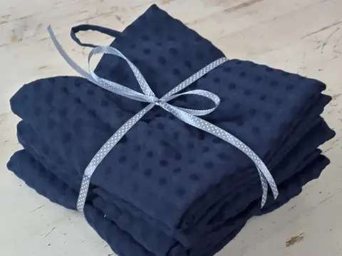 A stack of folded dark blue tea towels tied with a pale ribbon on a whitewashed table.