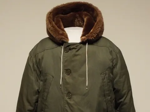 An olive green padded parka with a fur-lined hood displayed on a mannequin torso against a plain wall.