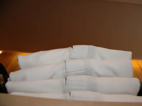 A stack of folded white pique polo shirts on a shelf.
