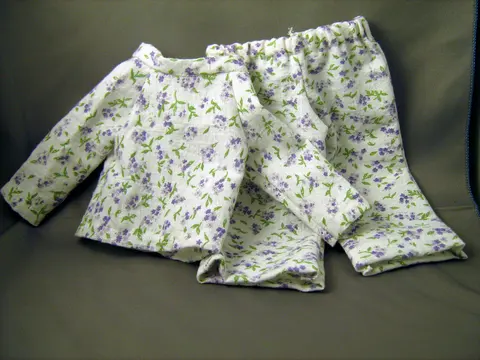 A white floral cotton pyjama set with a long-sleeved top and trousers lying flat on dark fabric.