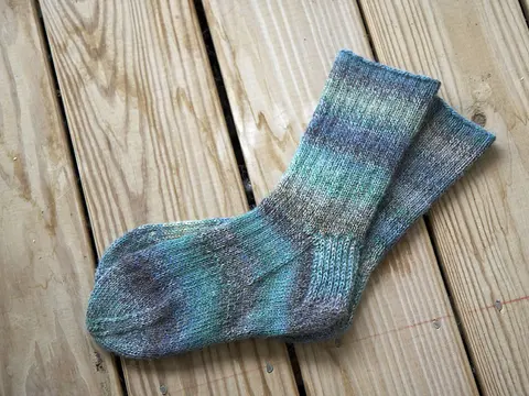A pair of striped hand-knitted socks laid on wooden decking.