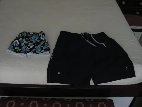Two pairs of swim shorts, one floral and one plain navy, laid flat on a bed.