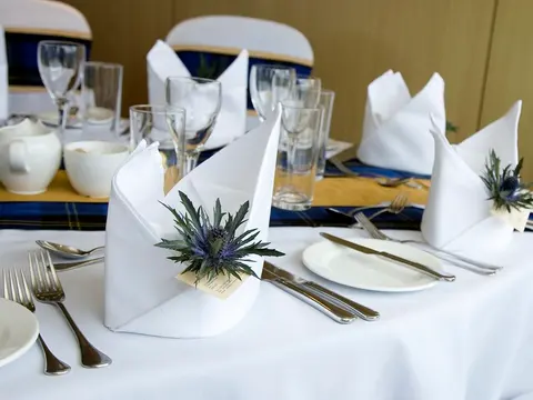 A white tablecloth laid with folded white napkins, cutlery, plates and glasses.