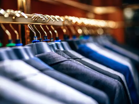 Navy and grey blazers hanging in a row on brass hangers, with small size markers on the hanger necks.