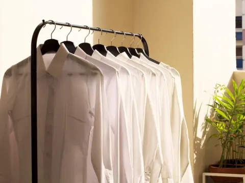 A row of plain white collared work shirts hanging on black hangers on a garment rail.