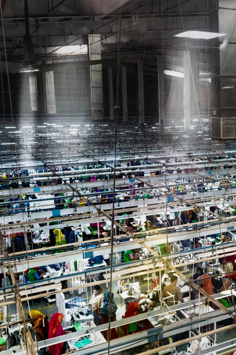 A large garment factory sewing floor seen from above with long rows of machines.