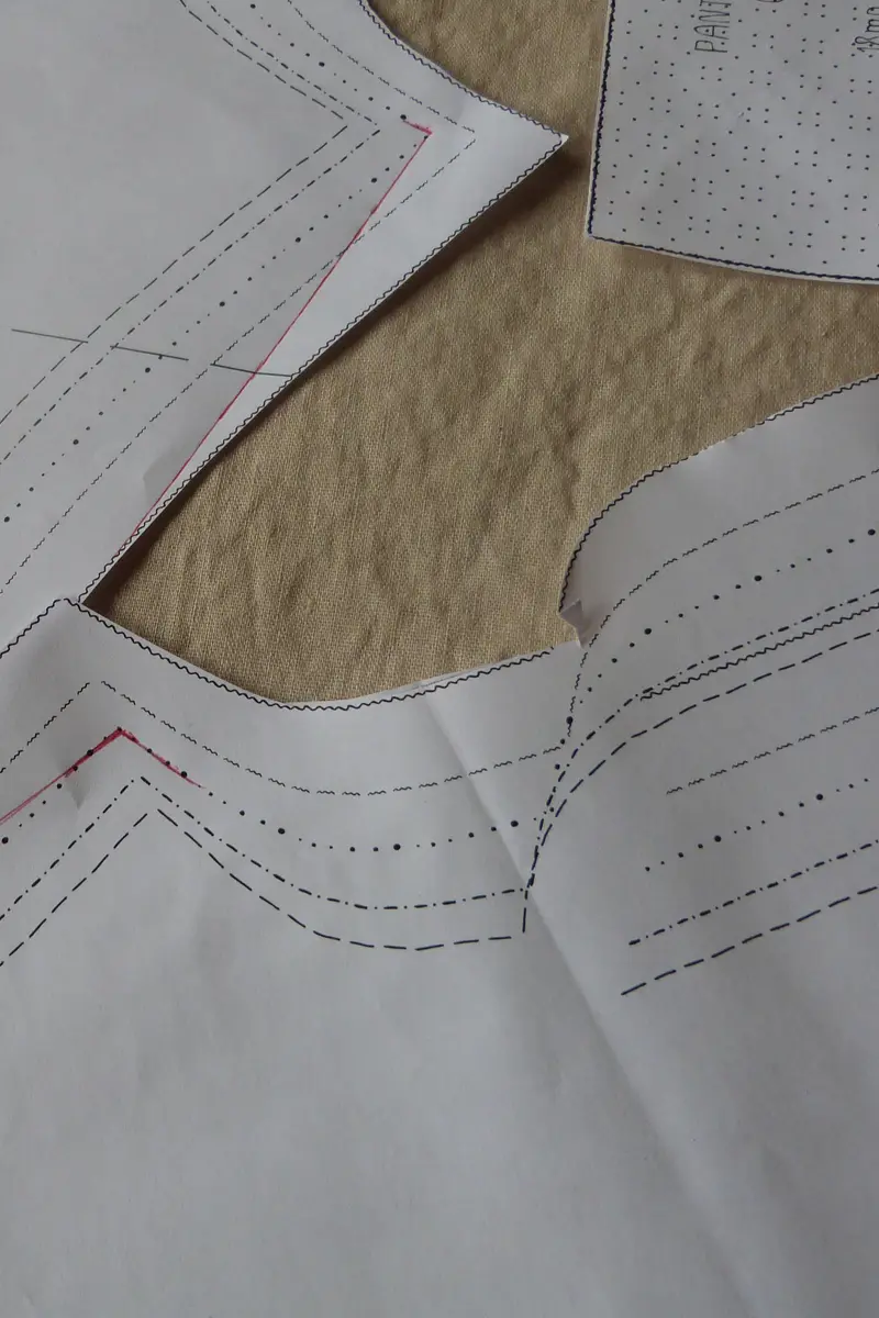 Paper sewing pattern pieces laid out on beige fabric ready for cutting.