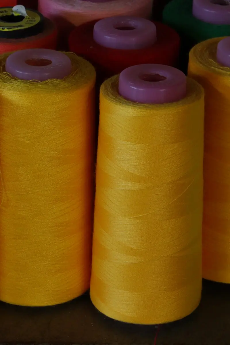 Rows of sewing-thread cones in yellow, green, pink and red standing close together on a dark shelf.
