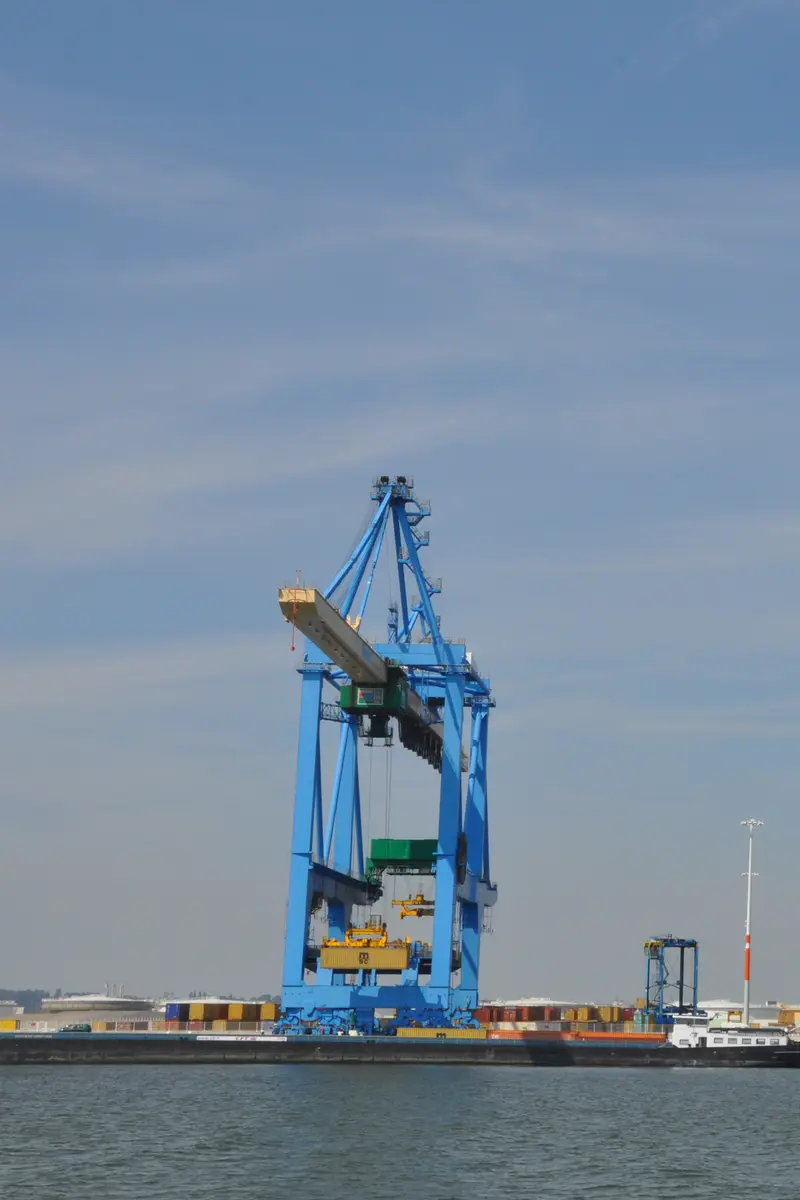 Three blue container cranes on a quay above stacked containers under a clear sky.