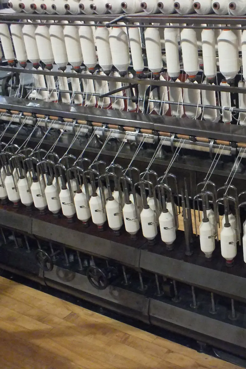 Rows of white yarn bobbins on a ring spinning frame inside a textile mill.