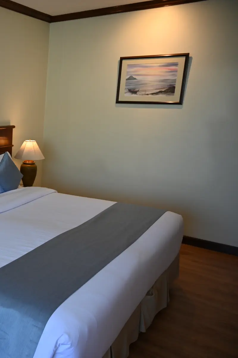 A neatly made hotel bed with white linen, a grey runner and two bedside lamps.
