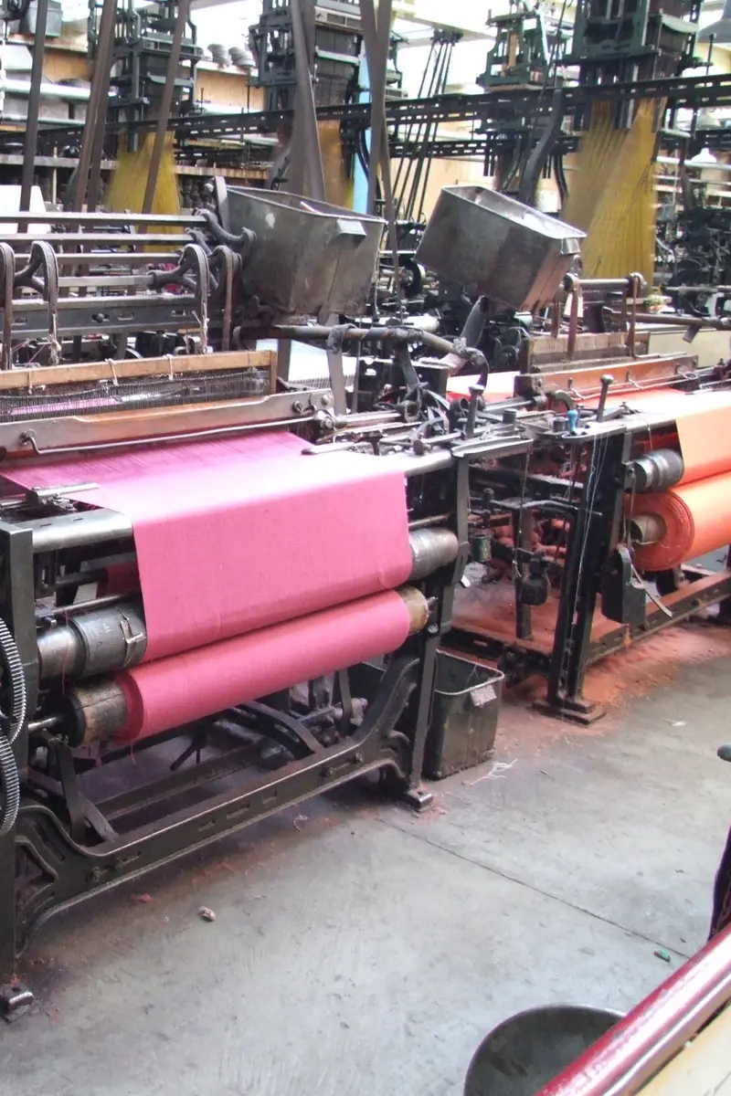 Rows of old power looms in a weaving shed with pink cloth on the nearest loom.