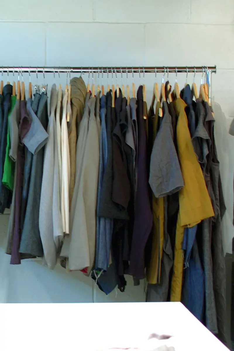 Shirts and jackets in muted colours hanging on a chrome rail beside a dress form.
