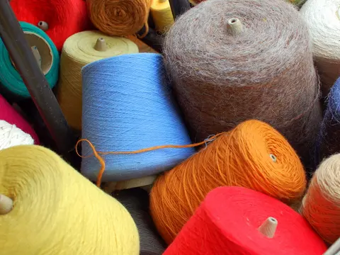 Cones of dyed yarn in red, orange, blue, yellow and other colours stacked together.