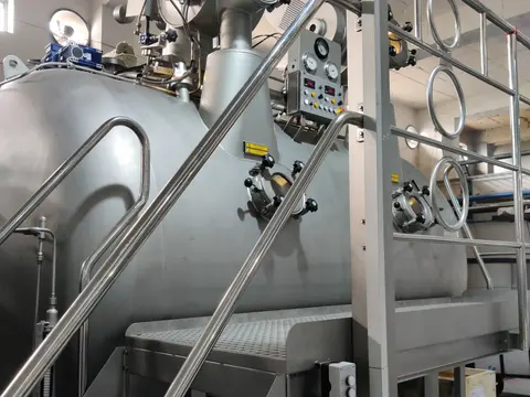 Stainless steel fabric dyeing machine with its control panel, access platform and inspection ports inside a dye house.