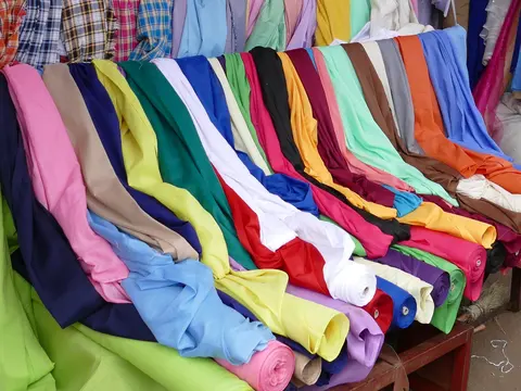 Rolls of plain dyed cotton fabric in bright pinks, greens, blues, yellows and reds laid out on a market stall.