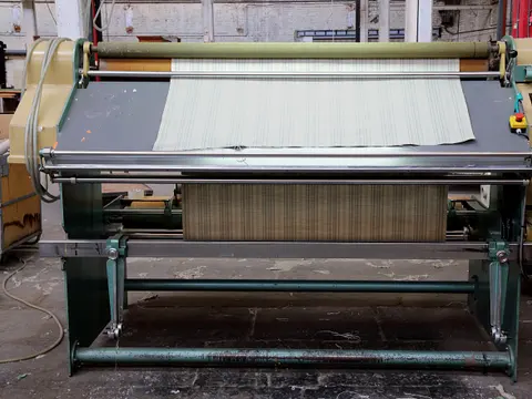 Fabric inspection machine in a mill with a length of striped cloth drawn over its lit viewing table.