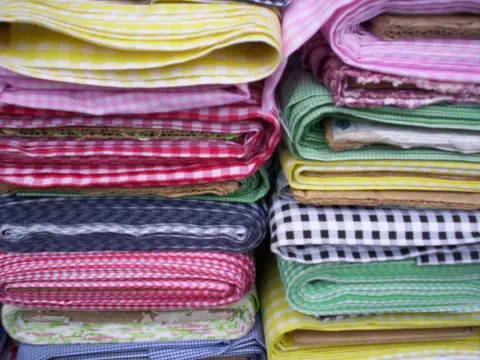 Folded bolts of gingham check shirting fabric in red, pink, yellow, green, navy and black stacked in a shop.