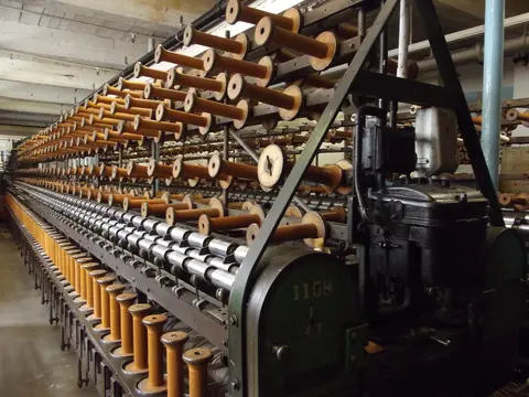 Long rows of wooden bobbins loaded on a spinning frame inside a textile mill.