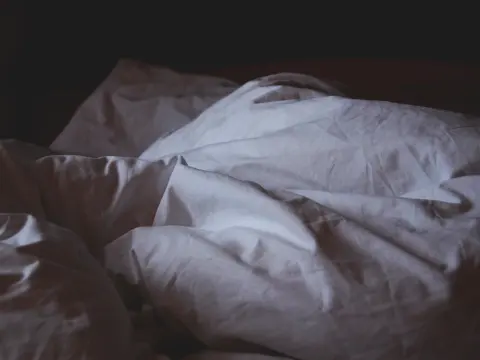 Soft folds of a white cotton bed sheet in low light.